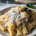 Ein Teller mit cremiger Pasta, zarten Blumenkohlröschen und gewürfeltem Schinken in einer hellen Sahnesauce, garniert mit einer Schicht goldbraun gerösteter, knuspriger Brösel