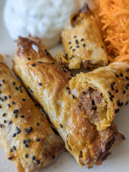 Knusprige Stangen Börek mit Hackfleisch auf einem Teller, bestreut mit Schwarzkümmel, daneben Tzatziki und Karottensalat