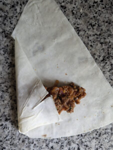 Die Füllung vom Stangen Börek wird im Teig eingeklappt, damit man sie einrollen kann